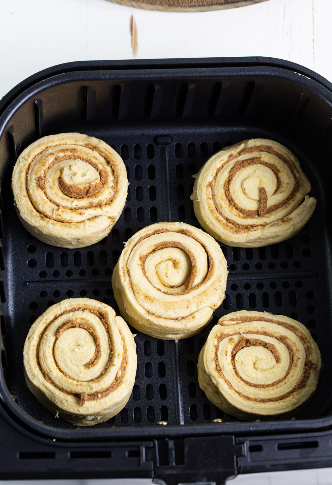 Uncooked cinnamon rolls in air fryer basket.