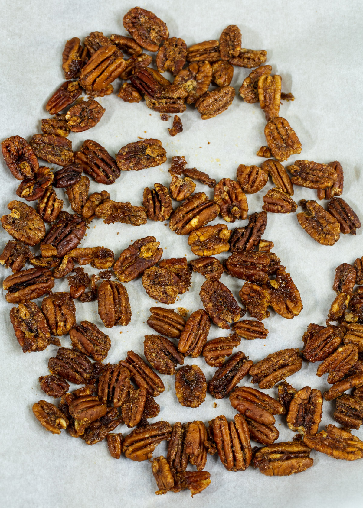 Glazed pecans spread out on parchment paper.