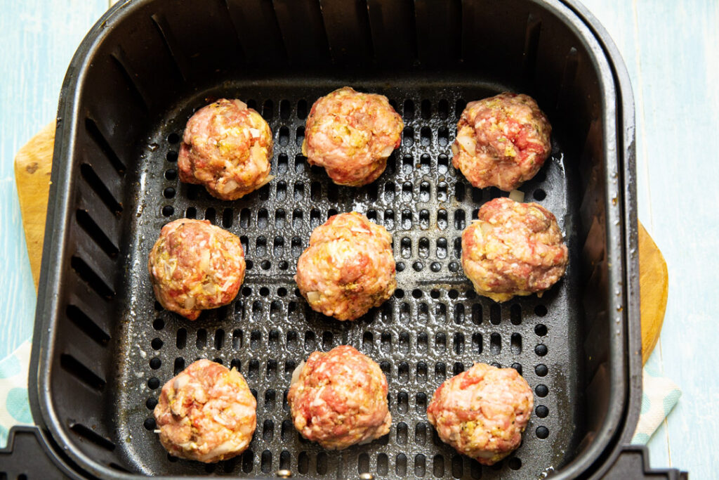 Uncooked meatballs in air fryer basket.