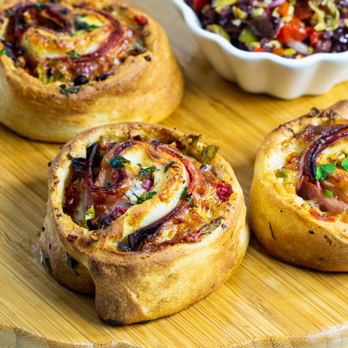 Air Fryer Muffaletta Pizza Rolls on a wooden board.