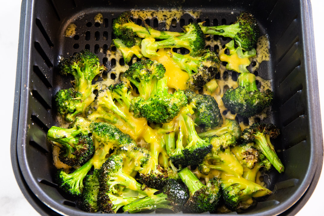 Broccoli topped with cheese in air fryer basket.