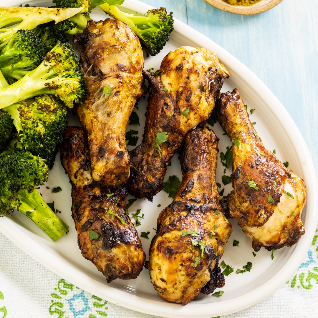 Air Fryer Crispy Curry Drumsticks on serving plate with broccoli.