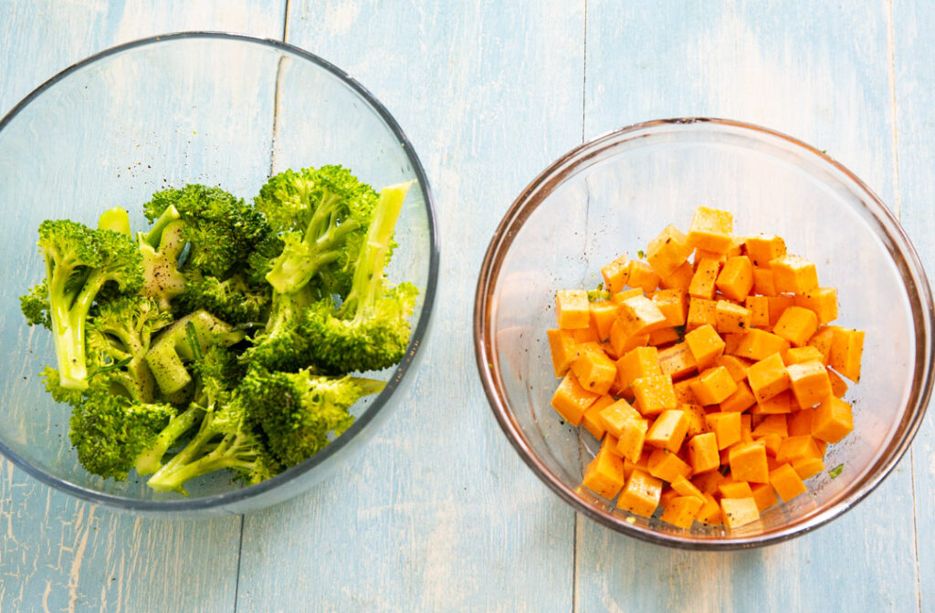 Broccoli florets in a bowl and sweet potato cubes in a bowl.